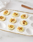 Deviled eggs on a decorative white plate with gold rim on a marble surface.