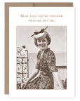 A vintage birthday card featuring a monochrome photograph of a smiling woman with a hat, accompanied by the text 'Rude that you're younger than me, but OK.' Wishing you a brilliant birthday.
