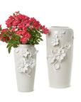 Two white vases with floral designs, one holding pink flowers on a white background