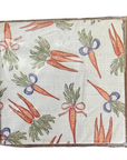A square fabric napkin with a brown border, featuring a repeating pattern of illustrated carrots in orange with green leafy tops and small blue ribbon accents, on a white background.