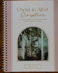 Notebook titled 'Christ in All of Scripture' on a wooden surface with a cup and glasses.