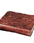 Brown leather-bound book with embossed design on a plaid fabric background