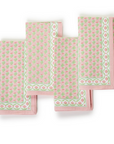 A set of four pink cloth napkins with green and white floral block prints, displayed unfolded.