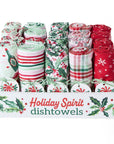 Christmas-themed dishtowels rolled up and arranged in a white display box. The towels feature festive holiday patterns including stripes, holly, snowflakes, and plaid in red, green, and white.