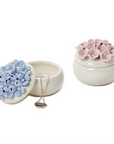 Two hand-painted porcelain jewelry boxes, one in blue and the other in pink, each with a floral design resembling hydrangea blooms on top.