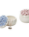 Two hand-painted porcelain jewelry boxes, one in blue and the other in pink, each with a floral design resembling hydrangea blooms on top.