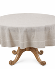 A round dining table covered with a light beige linen tablecloth, set against a plain white background.
