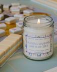 Candle in a jar labeled 'Playing Mahjong with Mah Girls' on a mahjong board.