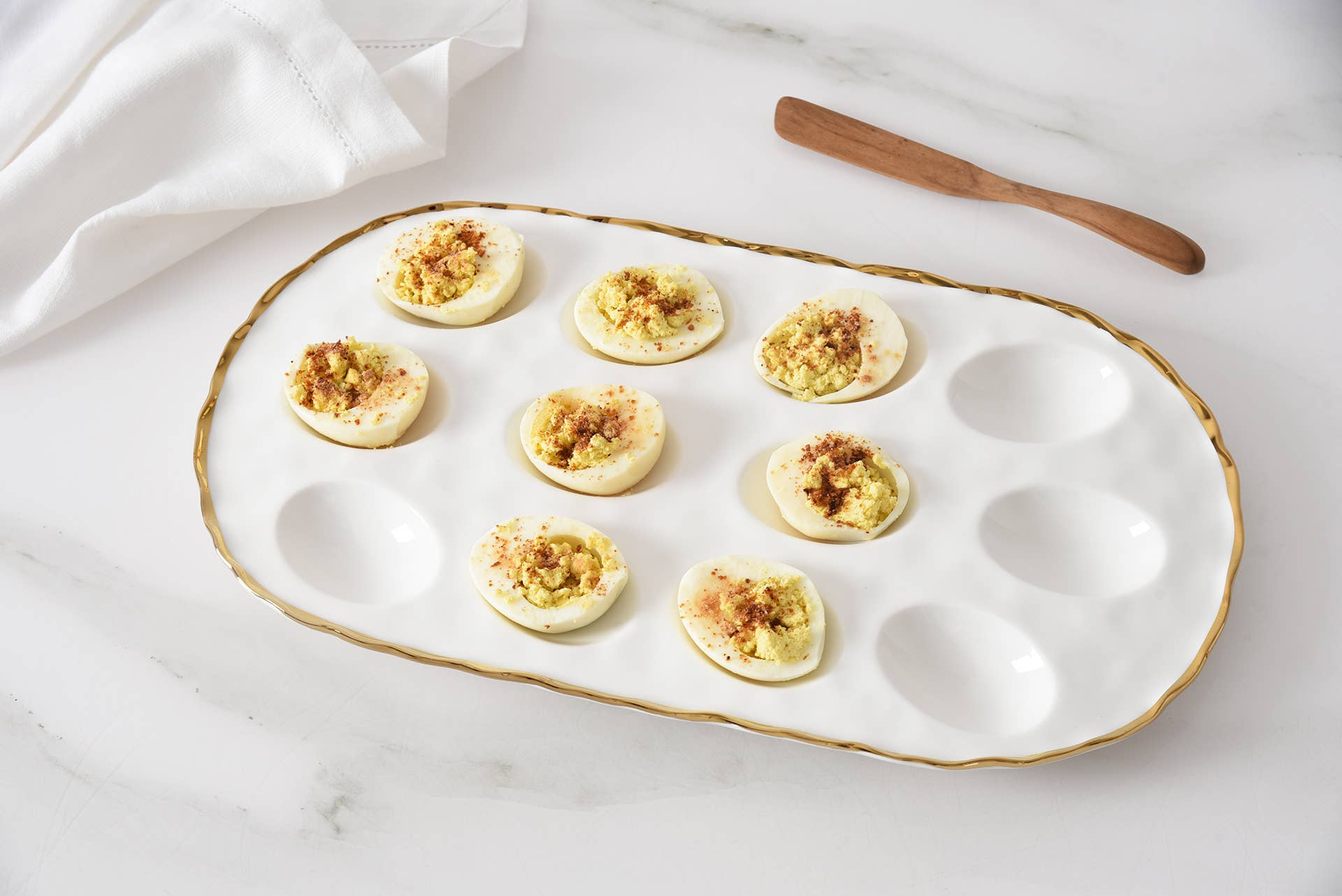 Deviled eggs on a decorative white plate with gold rim on a marble surface.