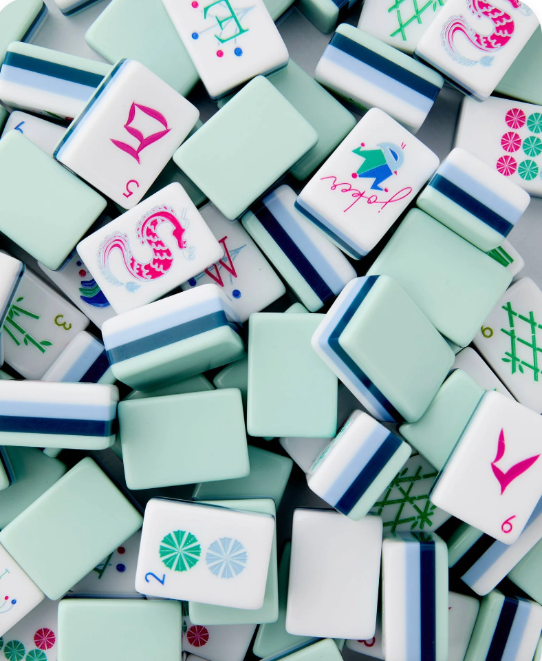 A close-up pile of white mahjong tiles with mint green, navy blue, and pastel accents, filling the frame.