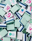 A close-up pile of white mahjong tiles with mint green, navy blue, and pastel accents, filling the frame.