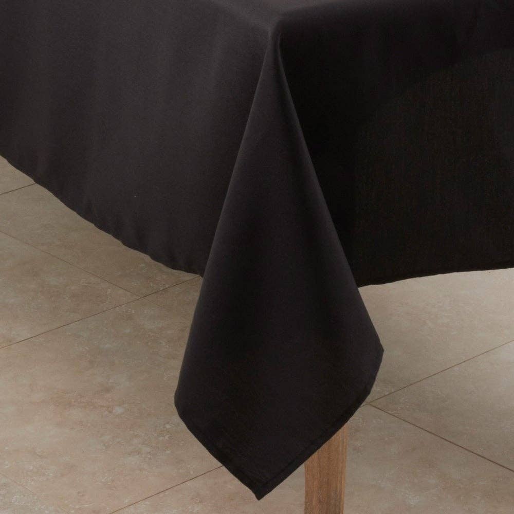 A black tablecloth draped over a table corner, hanging down in a triangular drape over a light wood table leg.