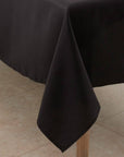 A black tablecloth draped over a table corner, hanging down in a triangular drape over a light wood table leg.