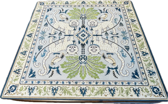 An ornate square area rug with a detailed botanical and animal motif, featuring a light blue field, cream borders, green leaves, and blue accents.