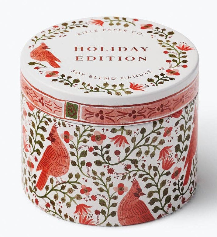 A round tin candle labeled 'Holiday Edition' with a white lid and a white body decorated with red birds and green foliage, photographed on a clean white background.