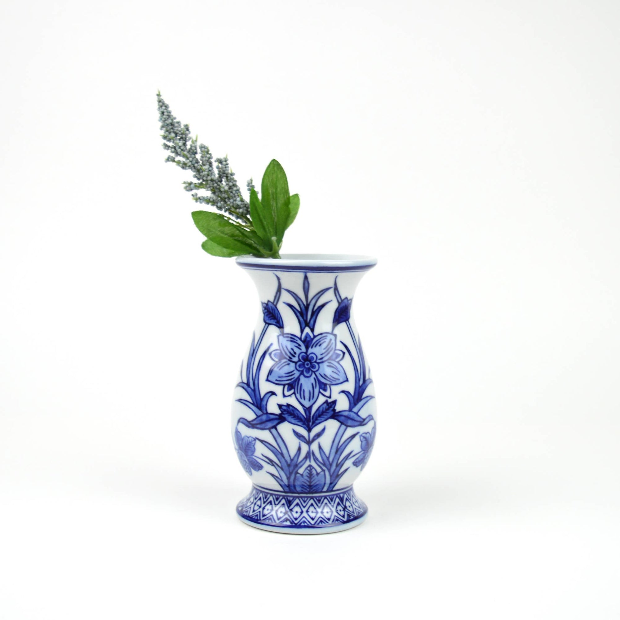 A blue and white porcelain Chinoiserie-style bud vase with a floral pattern, containing a sprig of greenery.