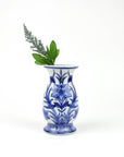 A blue and white porcelain Chinoiserie-style bud vase with a floral pattern, containing a sprig of greenery.