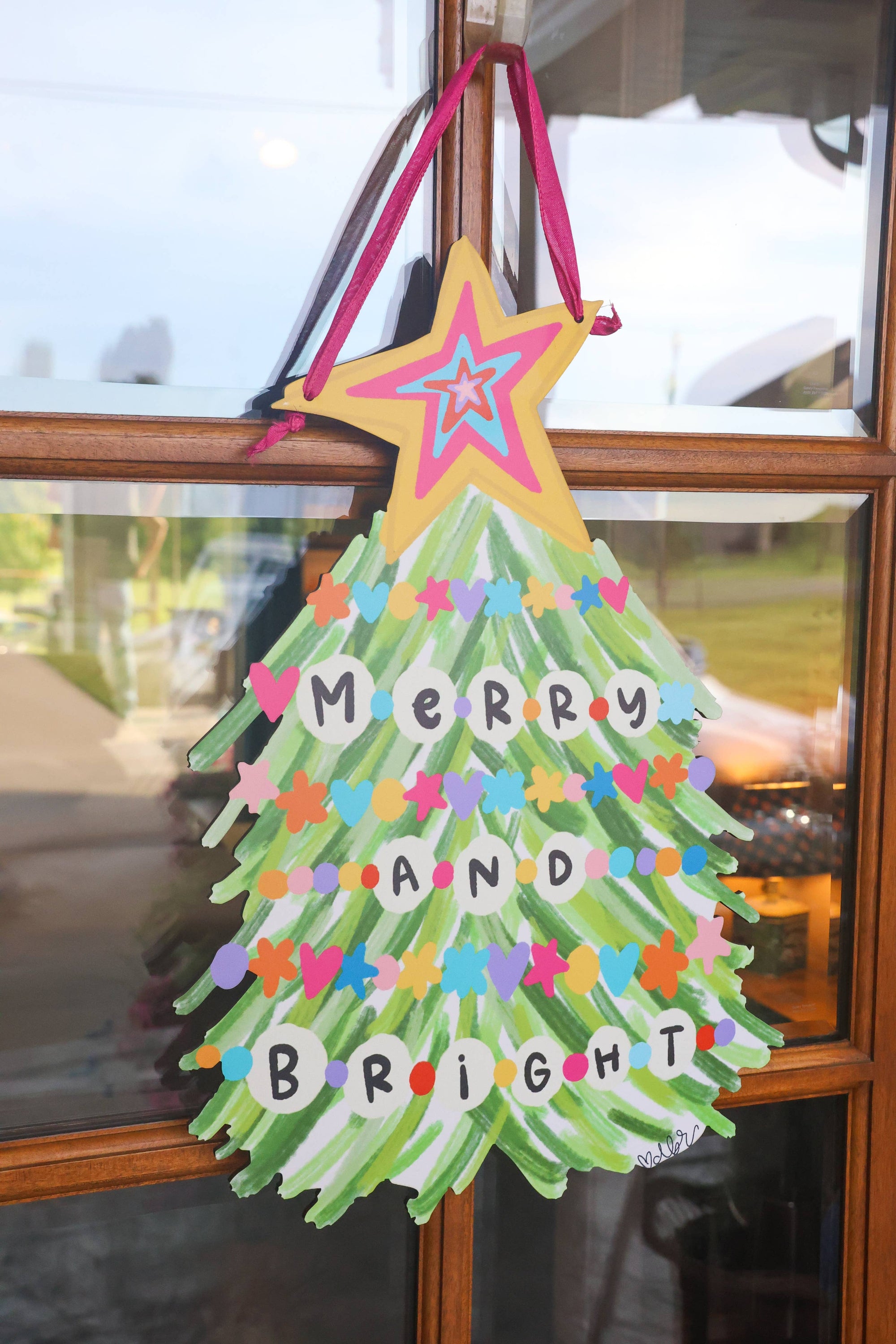 Decorative Christmas tree sign with colorful stars and 'Merry and Bright' text on a glass door.
