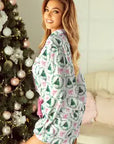 Woman in a festive pajama set standing next to a decorated Christmas tree.
