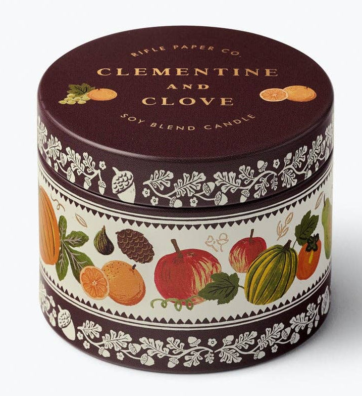 A round metal tin candle with a dark brown lid and a decorative label featuring illustrations of citrus fruits and botanical patterns, labeled 'CLEMENTINE AND GLOVE' by 'Belle Epoque Candles'.