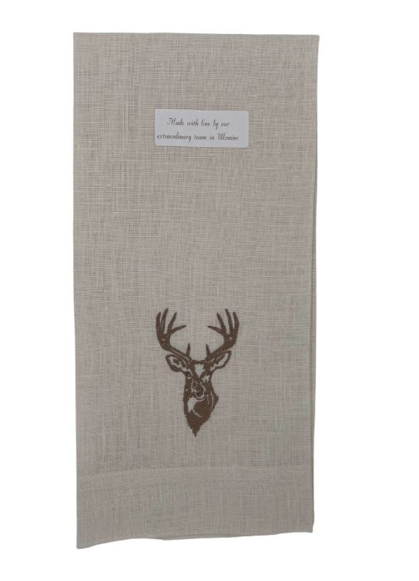 A beige linen towel with a brown embroidered stag design at the top and a text label indicating the brand.