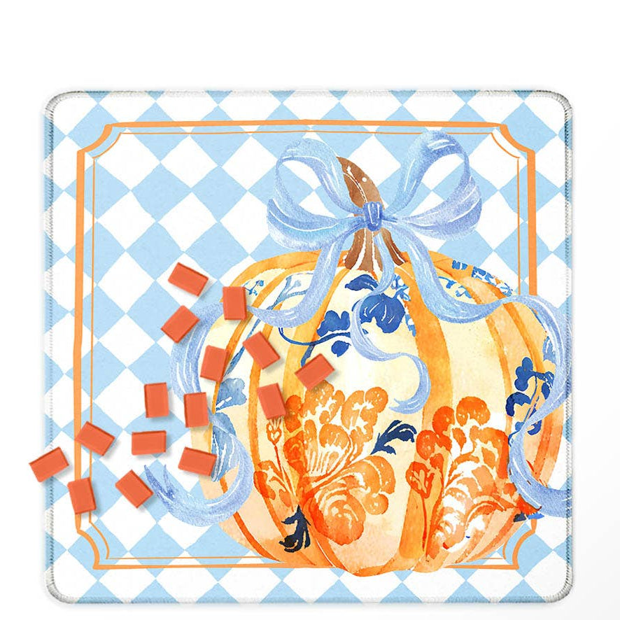 A Mahjong mat featuring a decorative autumn illustration. The design shows a large orange watercolor pumpkin with blue floral details and a blue ribbon bow, set against a light blue and white checkered background with an orange border.