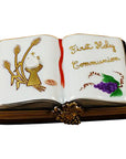 A hand-painted porcelain Limoges box depicting a book with 'First Holy Communion' text and religious symbols, measures 2.5 inches by 1.