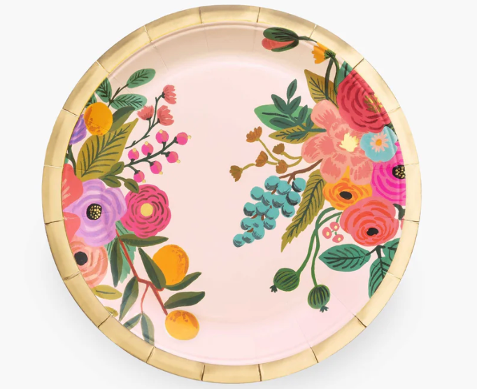 A round paper plate with a light pink background and a colorful floral print, featuring a gold-colored ridged rim, shown against a plain white background.