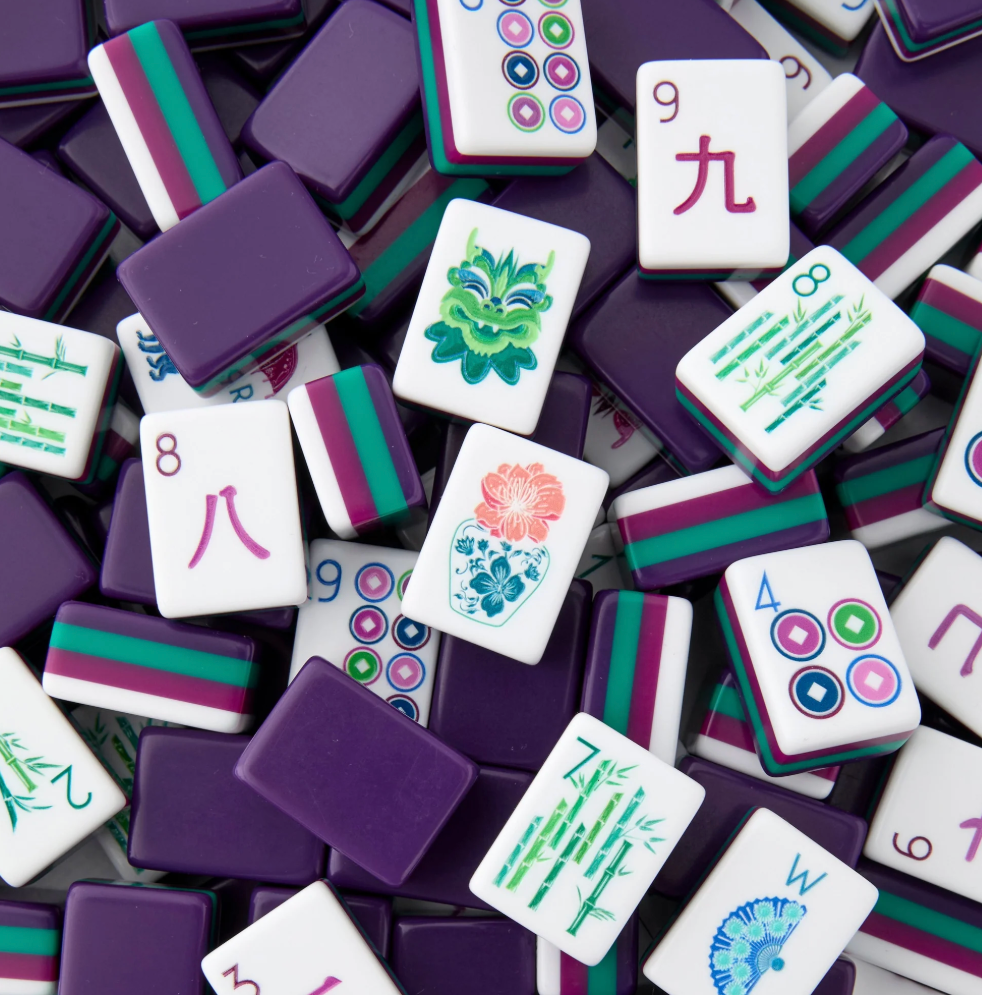 A pile of Mahjong tiles with purple backs, green and magenta borders, and white faces featuring Chinese characters and floral patterns.