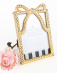 Gold bow-shaped picture frame with a pink rose on a white background