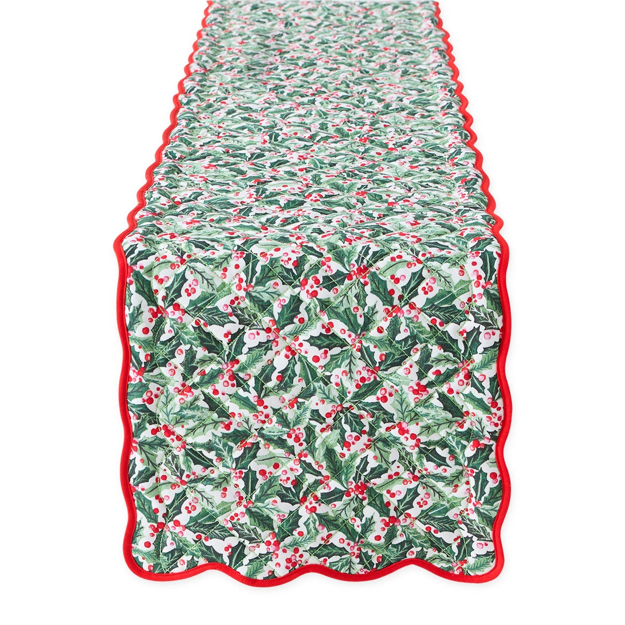 A quilted table runner with a festive holly and berry pattern in green, white, and red, finished with a scalloped red border, shown flat against a white background.