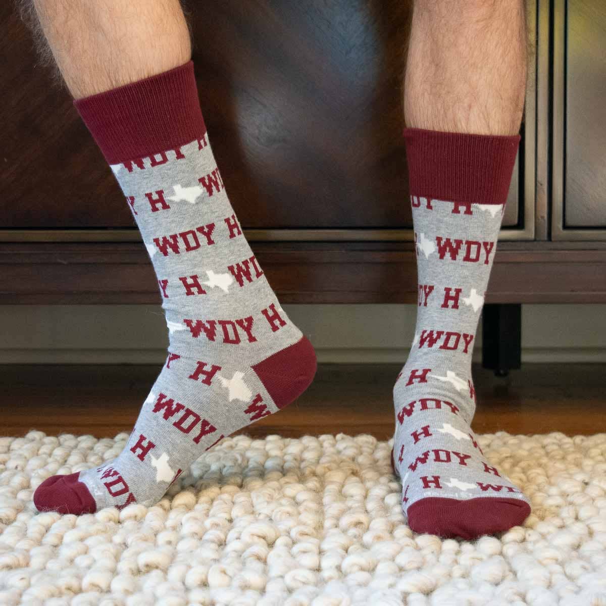Person wearing socks with 'Howdy' pattern on a carpeted floor.