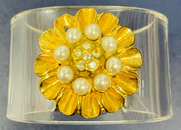 Clear cuff bracelet with a gold flower and pearl center on a gray background