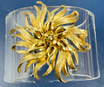 Gold flower-shaped brooch in a clear plastic case on a blue background