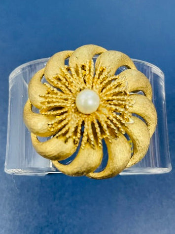 Gold flower-shaped ring with a pearl center on a blue background