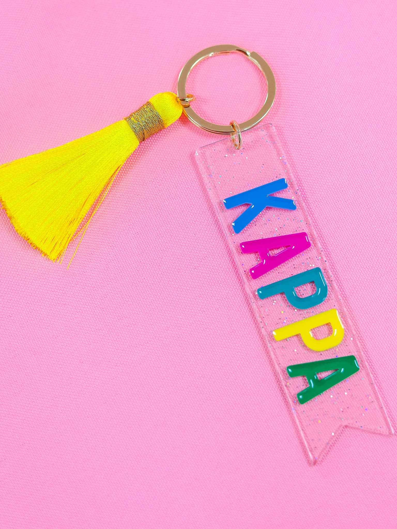 Keychain with 'Kappa' letters and yellow tassel on pink background