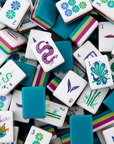A close-up pile of Mahjong tiles showing various symbols, numbers, and colors including teal, white, pink, green, and purple.