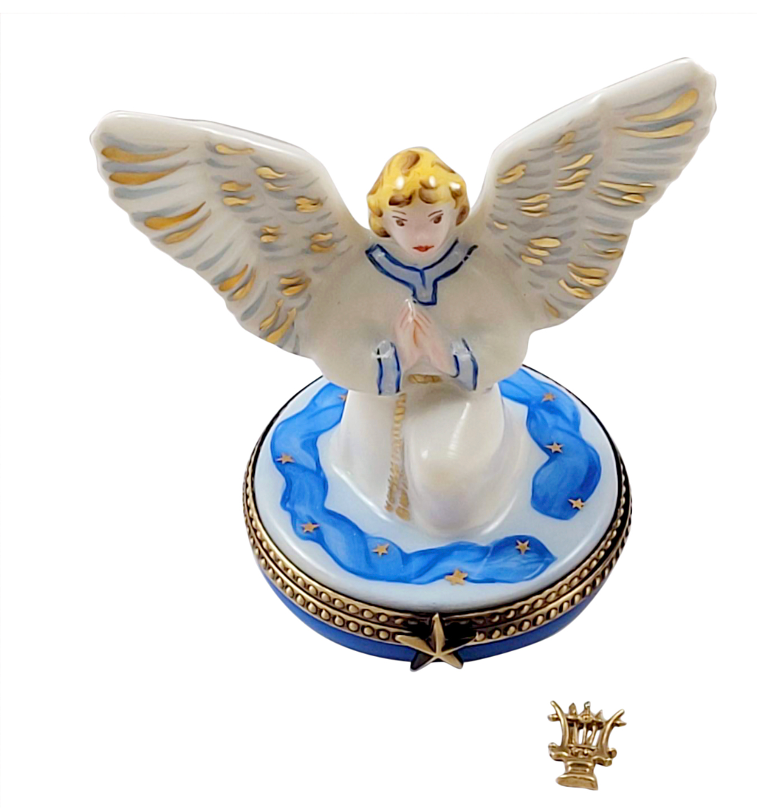 A porcelain angel figurine with outstretched wings standing on a decorated oval base, shown against a plain white background. A small crown-shaped accessory is placed below the main figurine.