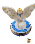 A porcelain angel figurine with outstretched wings standing on a decorated oval base, shown against a plain white background. A small crown-shaped accessory is placed below the main figurine.