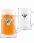 Two clear glass beer steins with white handles and a silver bull head emblem on the front, shown on a white background. The front stein is filled with orange beer and foam, while the rear stein is empty.