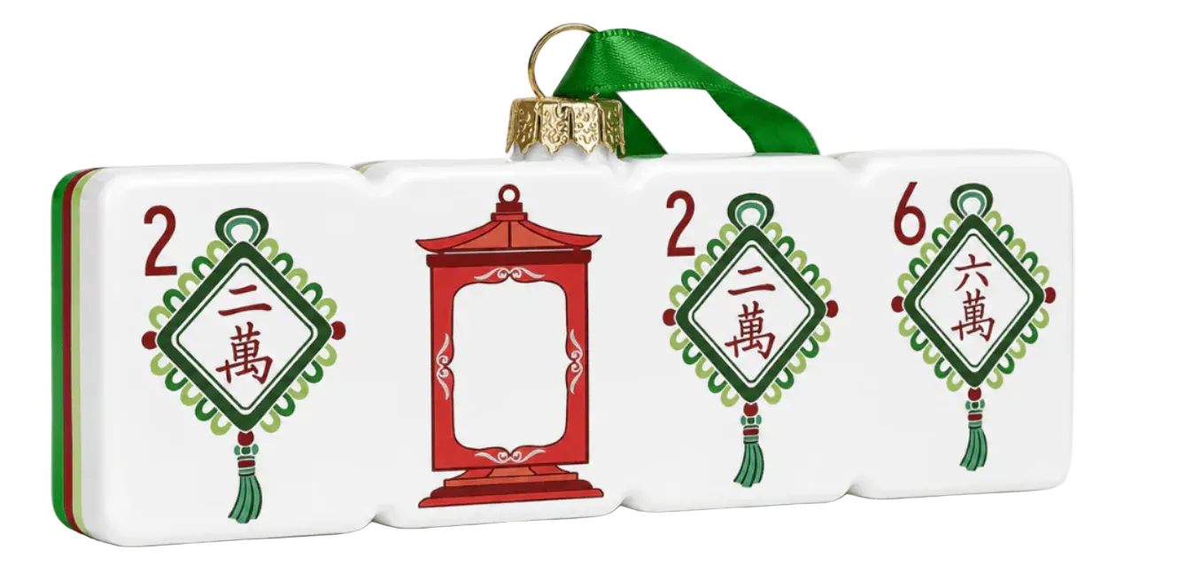 A decorative Christmas ornament shaped like a row of Mahjong tiles, featuring a green hanging ribbon at the top, white tile faces with red and green Chinese-style decorative motifs, and a red temple ornament in the center.