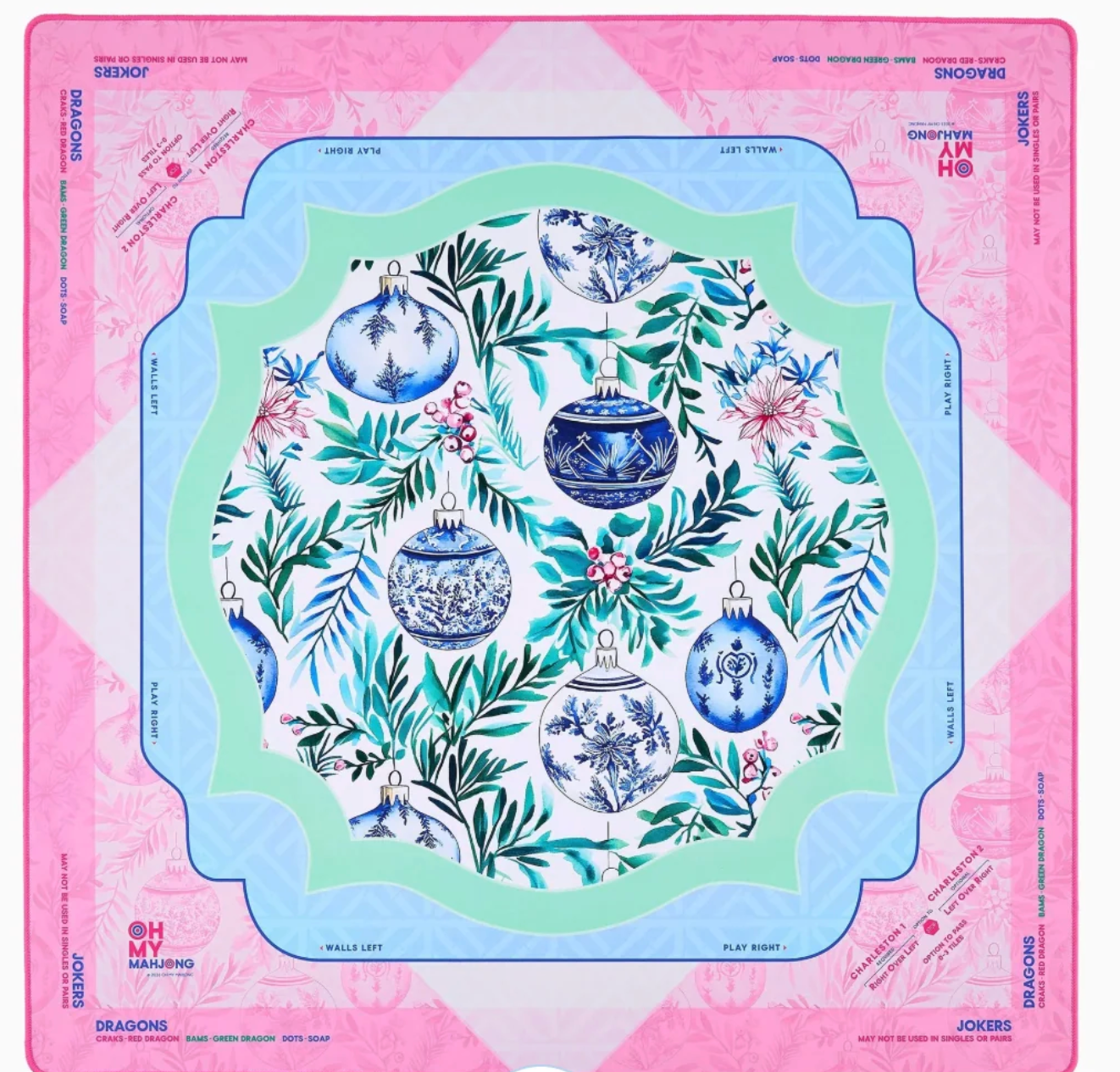 A Mahjong mat featuring a festive Christmas design with blue and white ornaments, green foliage, and pink flowers, framed by a pink and light blue border with brand text.