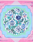 A Mahjong mat featuring a festive Christmas design with blue and white ornaments, green foliage, and pink flowers, framed by a pink and light blue border with brand text.