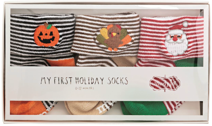 A boxed set of baby holiday socks labeled 'MY FIRST HOLIDAY SOCKS' showing three striped socks with embroidered seasonal faces: a pumpkin, a turkey, and Santa Claus.