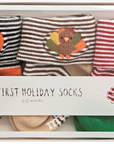 A boxed set of baby holiday socks labeled 'MY FIRST HOLIDAY SOCKS' showing three striped socks with embroidered seasonal faces: a pumpkin, a turkey, and Santa Claus.
