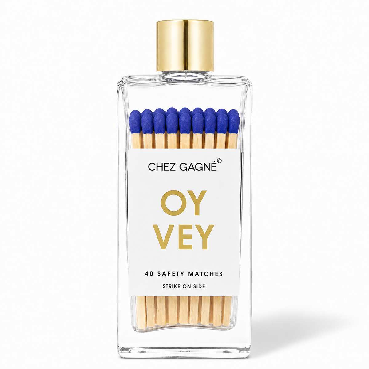 A clear rectangular glass bottle of Chez Gagne Oy Vey safety matches with a gold cap, white label, blue match heads, and visible wooden matchsticks inside, on a white background.