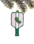 Decorative ornament shaped like a pickle on a green glittery base, hanging from a tree branch.