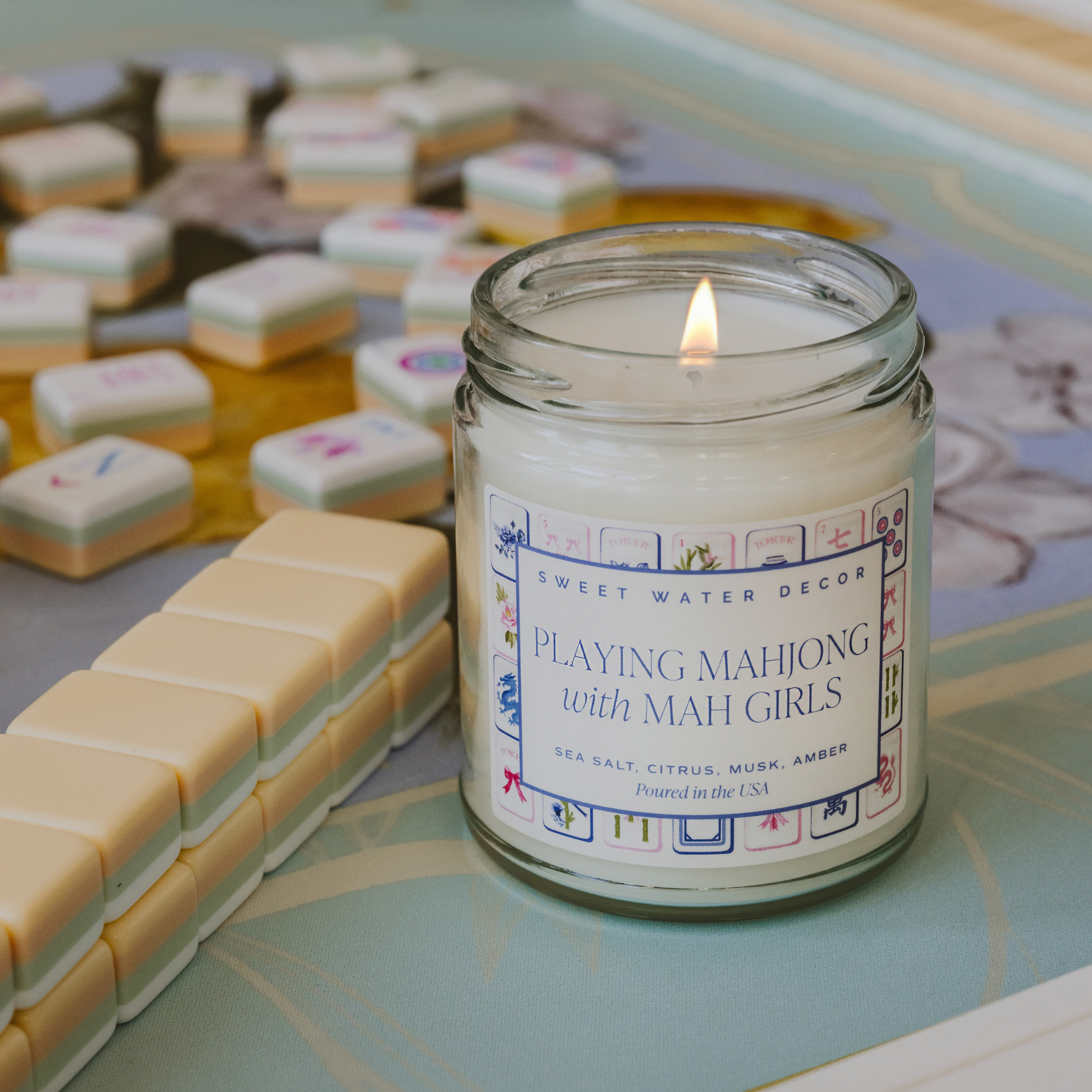 Candle in a jar labeled 'Playing Mahjong with Mah Girls' on a mahjong board.