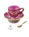 Pink ceramic cup and saucer set with a spoon and heart-shaped ball on a white background