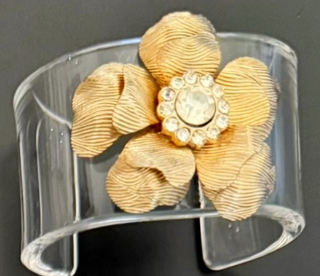 Gold flower-shaped bracelet on a clear stand against a black background